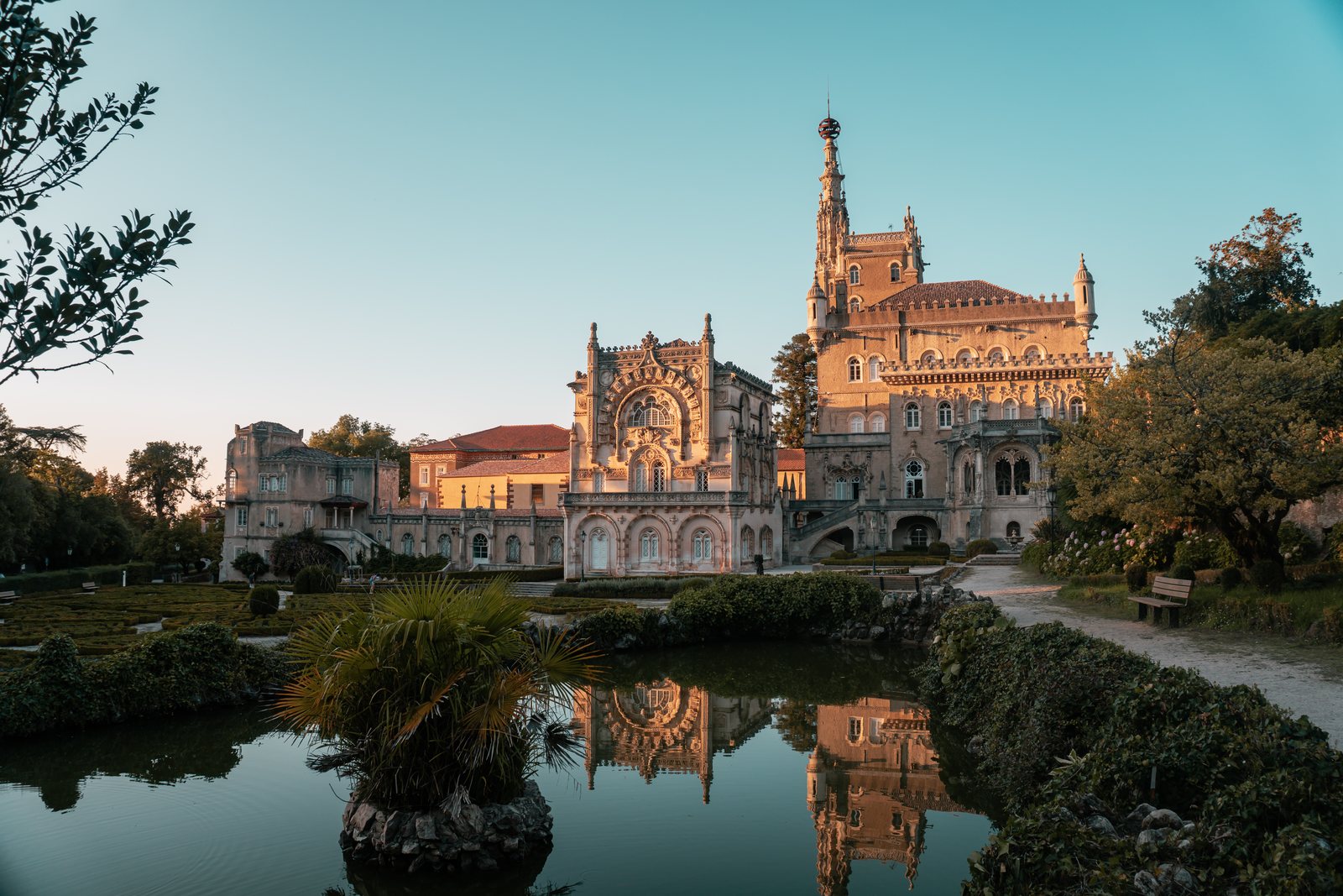 Ornate historic buildings and gardens reflected in a pond at golden hour
